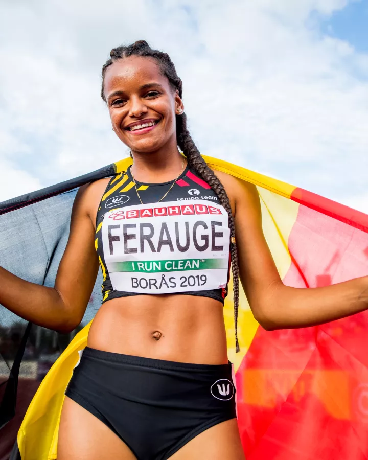 L'athlète belge Lucie Ferauge, souriante et portant fièrement le drapeau de la Belgique sur ses épaules, avec son dossard des championnats de Borås 2019.